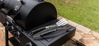 Oklahoma Joes heavy duty BBQ prep tools including tongs and spatula resting on a smoker