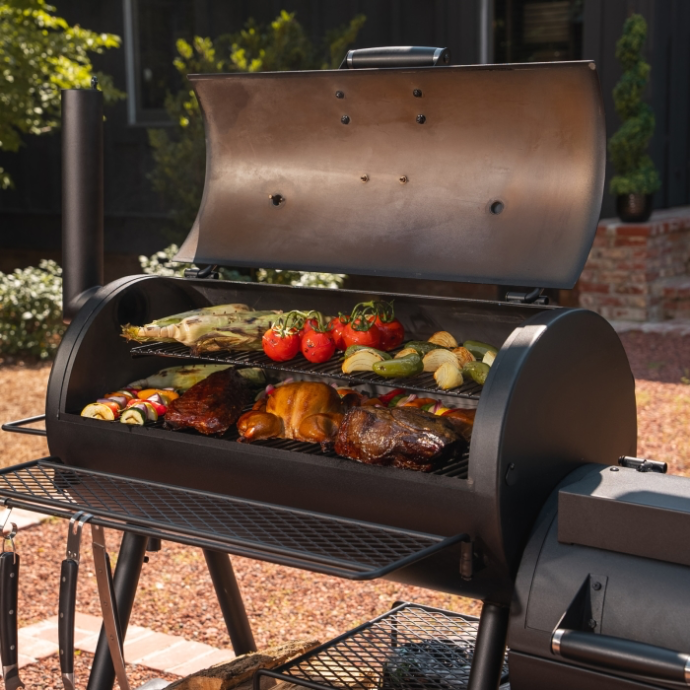 Oklahoma Joes traditional offset smoker loaded with slow cooked BBQ meat and vegetables