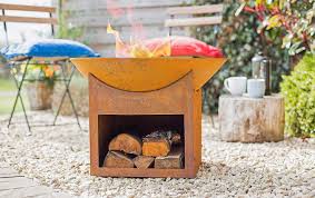 Orange outdoor fire bowl with logs and flames in a garden setting