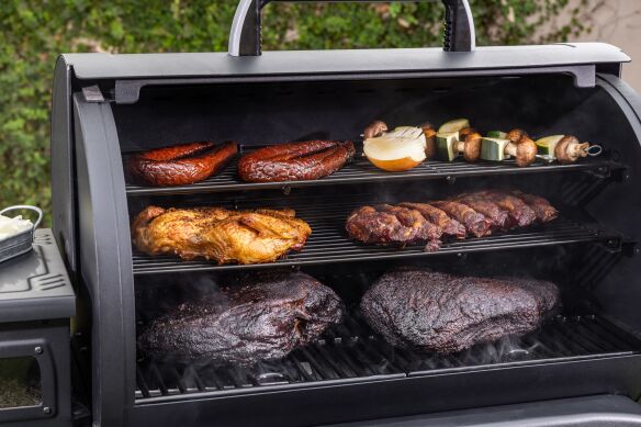 Brisket, pork ribs, and chicken smoking on multiple cooking racks inside a Pit Boss Competition Series grill