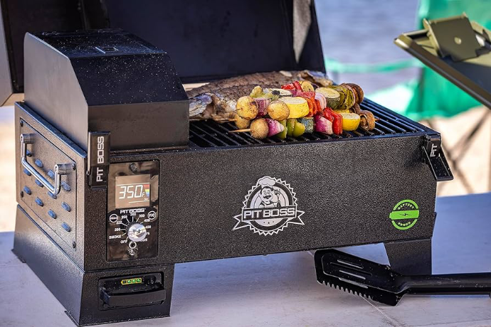 Tabletop Pit Boss portable pellet grill smoking a whole fish and colorful vegetable skewers outdoors